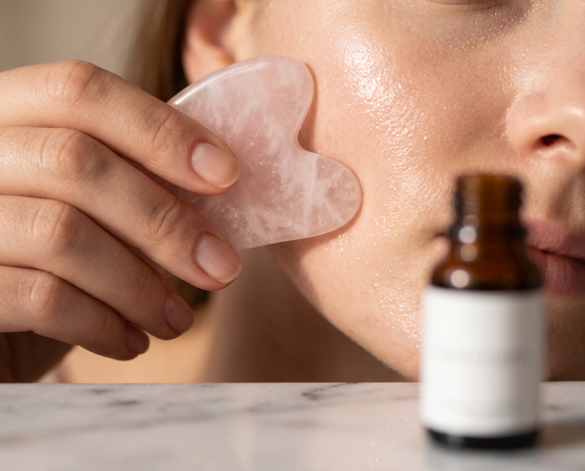Gros plan sur un gua sha en quartz rose glissé le long de la mâchoire